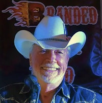 a man in a cowboy hat is smiling at a microphone